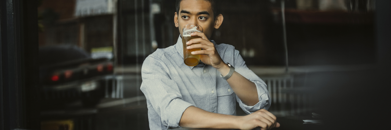 photo of a young man having a beer and looking out of a window