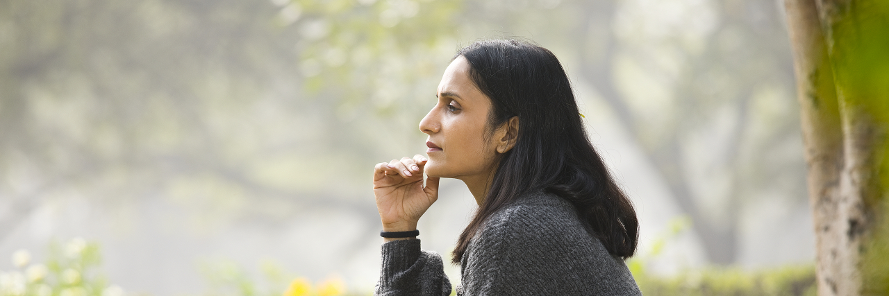 Person wearing gray sweatshirt sitting on a park bench, deep in thought.