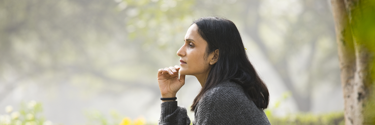 How My Seizures Have Shaped My Identity Person wearing gray sweatshirt sitting on a park bench, deep in thought.