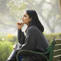 Person wearing gray sweatshirt sitting on a park bench, deep in thought.