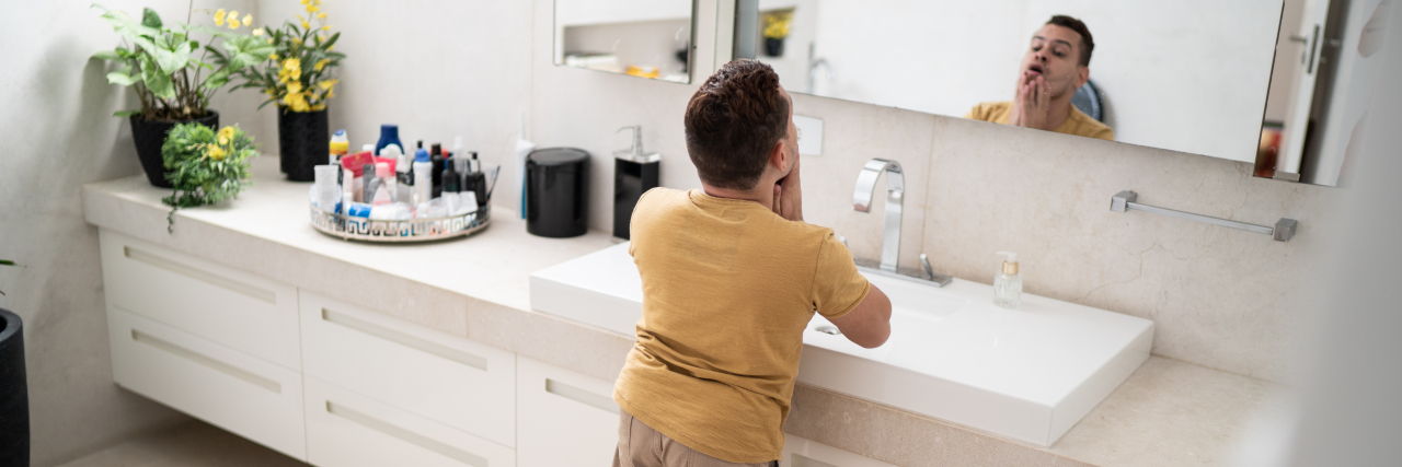 Breaking the 'Reach Barrier' for People With Dwarfism and Disabilities Young man with dwarfism looking in the mirror in the bathroom.