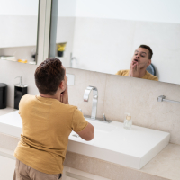 Young man with dwarfism looking in the mirror in the bathroom.