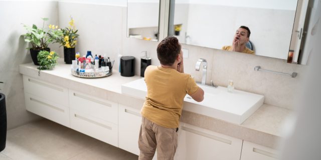 Young man with dwarfism looking in the mirror in the bathroom.