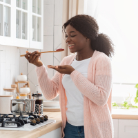 Cooking with chronic illness: Woman tasting food in the kitchen.