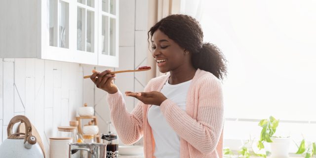 9 Spoonie Cooking Hacks to Save Time and Energy in the Kitchen Cooking with chronic illness: Woman tasting food in the kitchen.