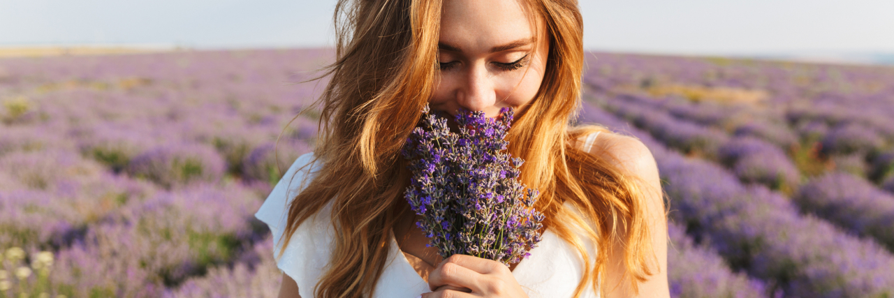 Photo of caucasian young woman in dress holding bouquet of flowers, while walking outdoor through lavender field in summer