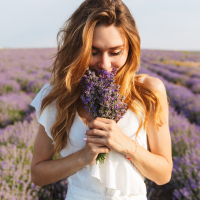 Photo of caucasian young woman in dress holding bouquet of flowers, while walking outdoor through lavender field in summer