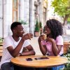 Portrait of stylish black couple talking to each other at summer street cafe.