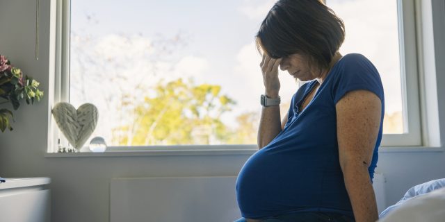 Mature pregnant woman sitting on her bed feeling ill.