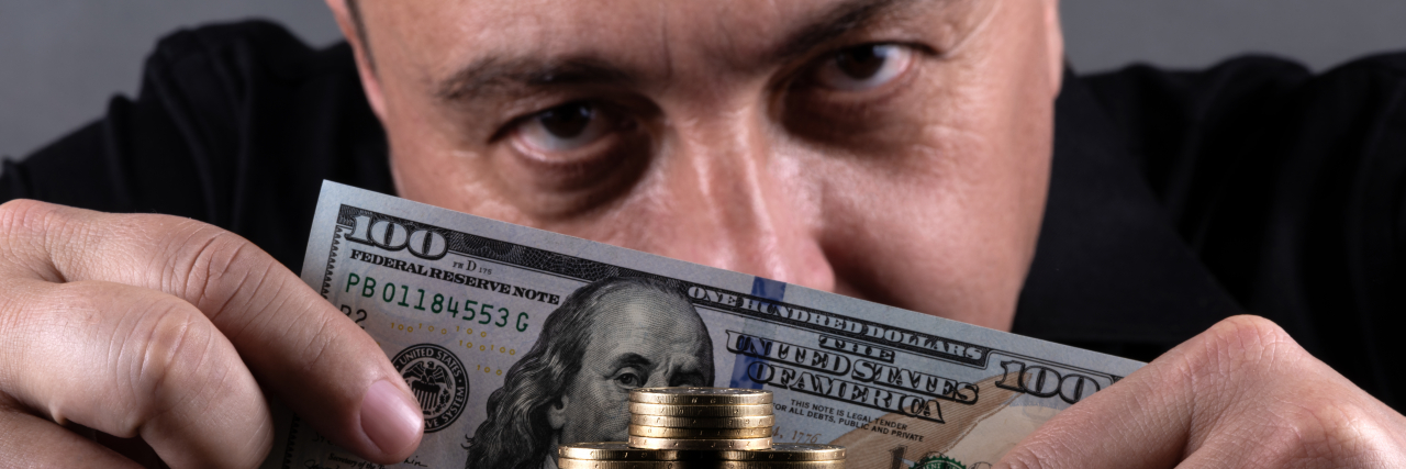 Social Security Disability Fraud Is Rare, Unlike These Common Scams Con artist holding a $100 bill in front of a stack of coins.