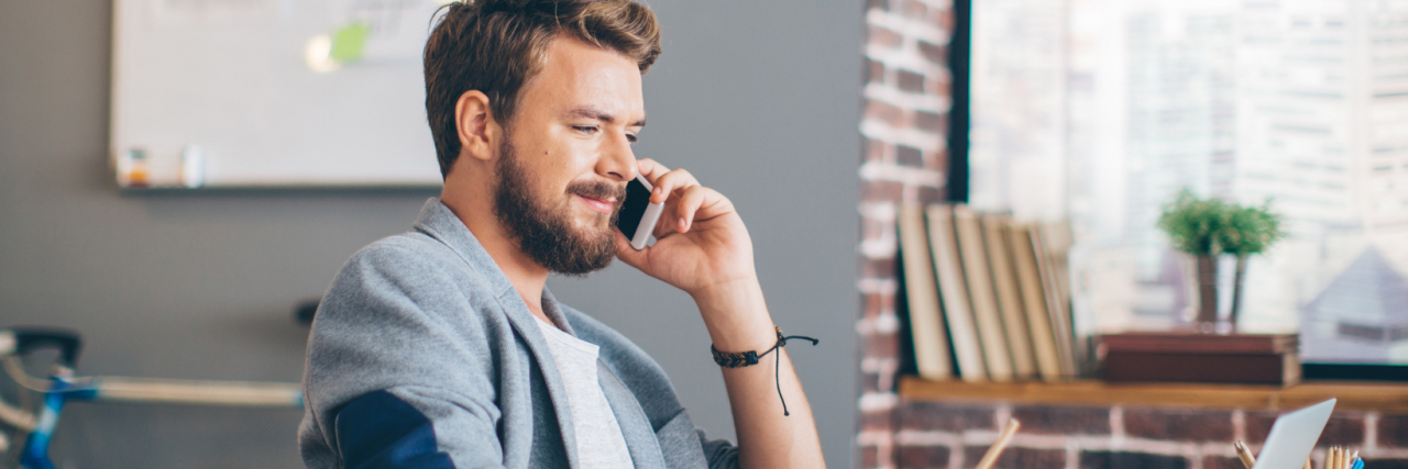 Mental Health Reasons Why Someone Might Overexplain photo of man sitting on the phone looking awkward or uncomfortable