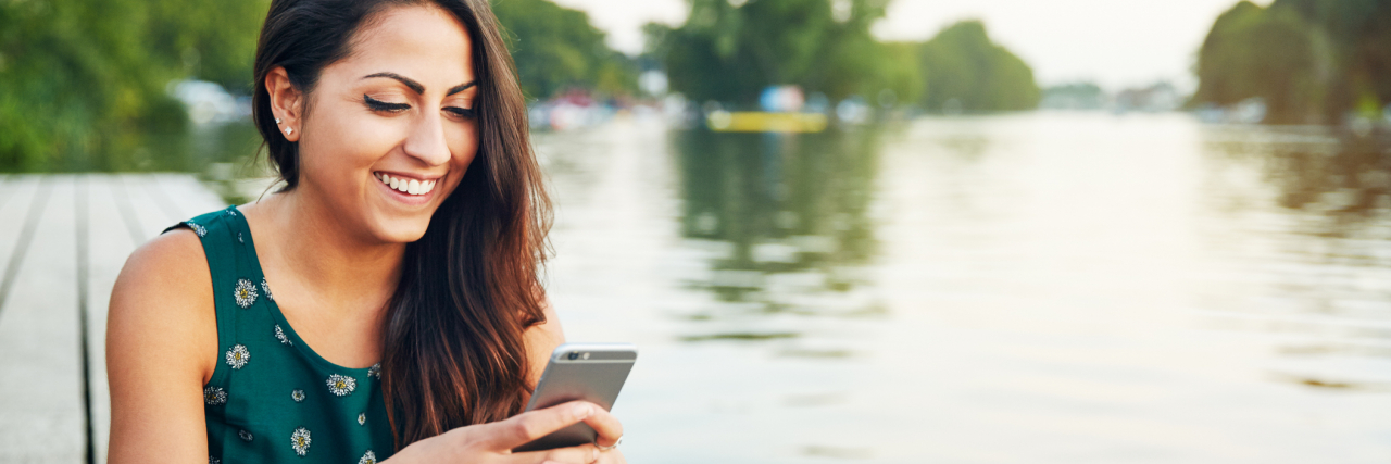 photo of a young person with a phone smiling beside a lake