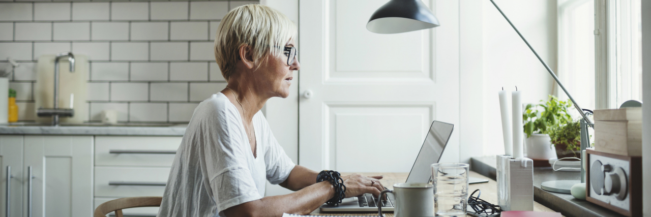 Older woman with short white hair sitting at a home desk, working remotely