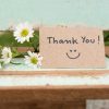 hank you note with smile face and flower cluster on wooden chair