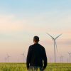 photo of a man on a green field with windmills in the distance, climate change and climate anxiety concept