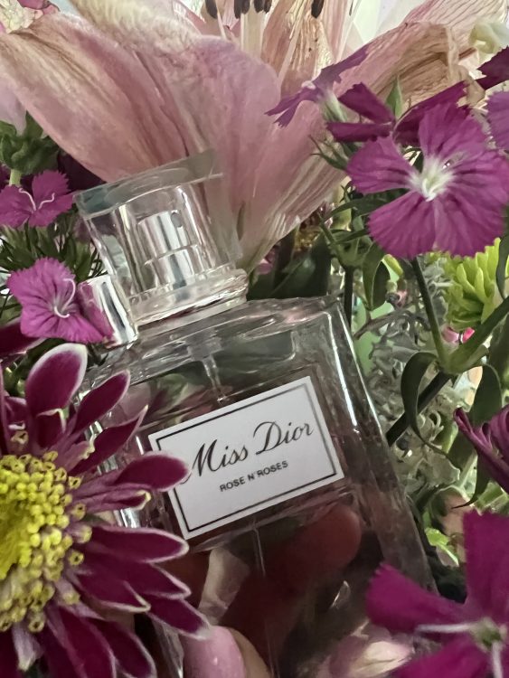 A bottle of Miss Dior Rose n Roses perfume with a bunch of flowers around it held by a pretty hand with cute nail polish