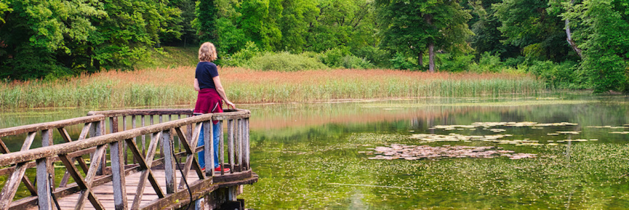Finding Comfort in the Stillness as a Trauma Survivor A woman standing on a doc looking out at the water