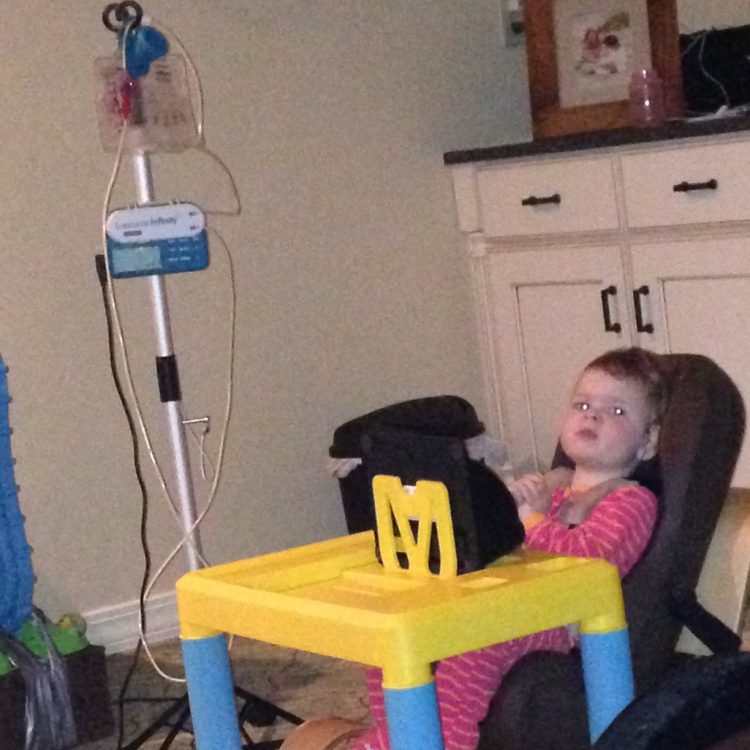 The author's daughter sits in a chair in front of a yellow and blue plastic table.