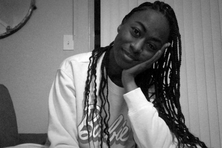 A very pretty very gorgeous Black girl with beautiful knotless box braids. It's me. I'm the Black girl in the image. She's wearing a Barbie sweatshirt and is leaning her head in her hand. I'm really cute.