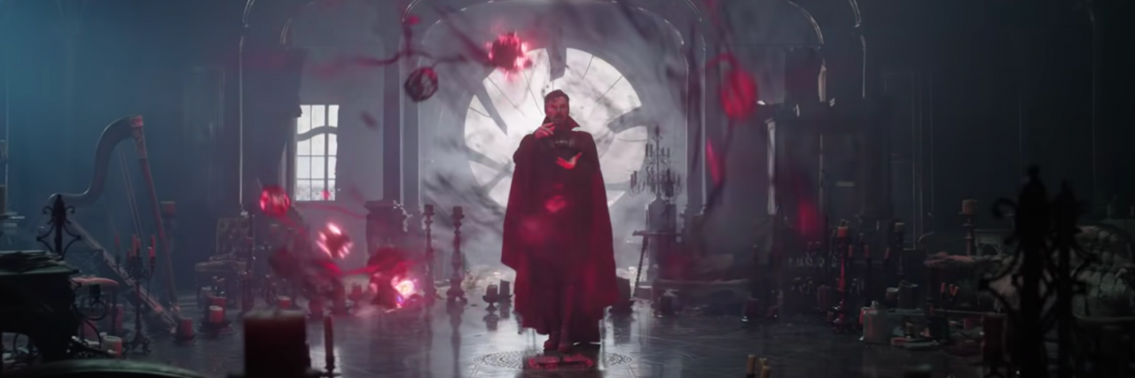 A screencap of Doctor Strange in The Multiverse of Madness where he's surrounded by red magic, candles, and a book