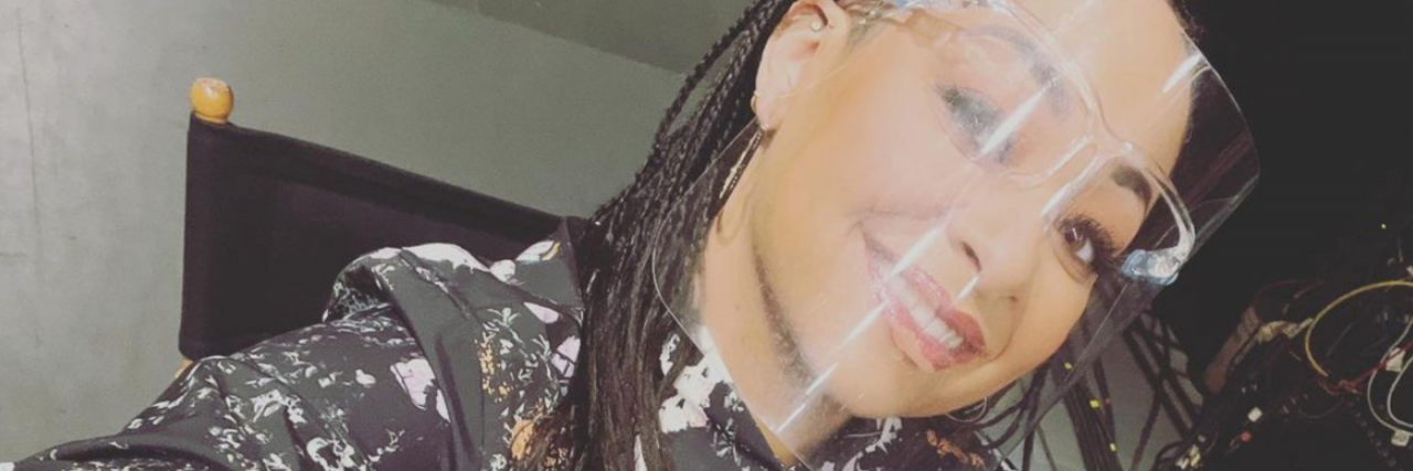 Raven-Symoné Says It's OK for Young People to Rest in Interview Raven Symoné smiles at the camera in a face shield in a shirt and sitting in a director's chair