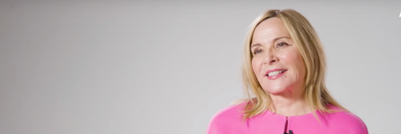 Kim Cattrall in bright pink sitting against a white background