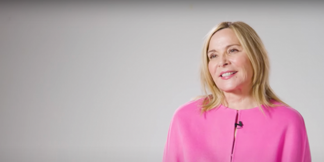 Kim Cattrall in bright pink sitting against a white background