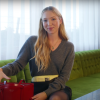 Lila Moss sitting on a big couch with a purse smiling at the camera
