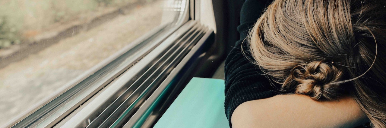 When Your Anxiety Manifests as Physical Symptoms Woman with her head down on table on train, next to window