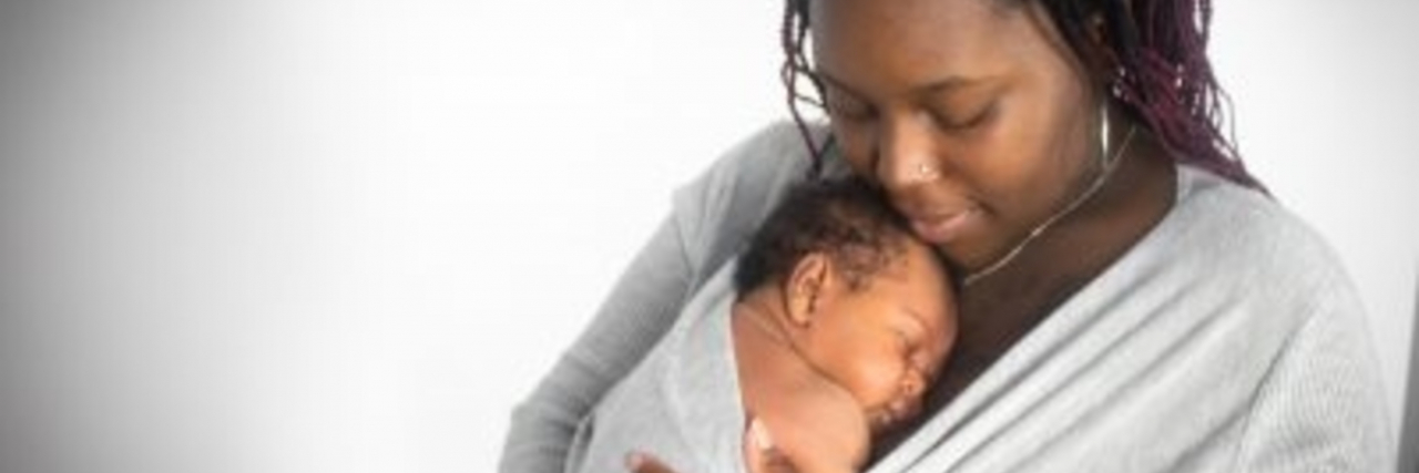 Accepting Your Physical Limitations as a Parent With Chronic Illness The author, a black woman holds her son in a swaddle in her arms.