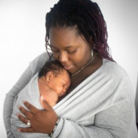 The author, a black woman holds her son in a swaddle in her arms.