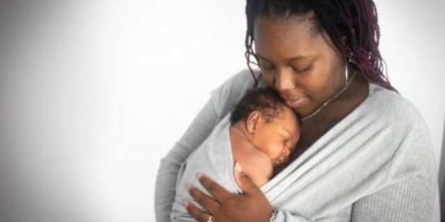 The author, a black woman holds her son in a swaddle in her arms.