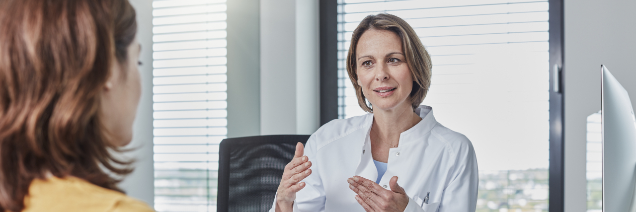 Lessons Learned in 10 Years of Living With Chronic Illness A female doctor talks to a woman with brown hair wearing a light orange top.