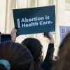 photo of a person holding a sign saying "Abortion is health care" at a protest in front of a government building