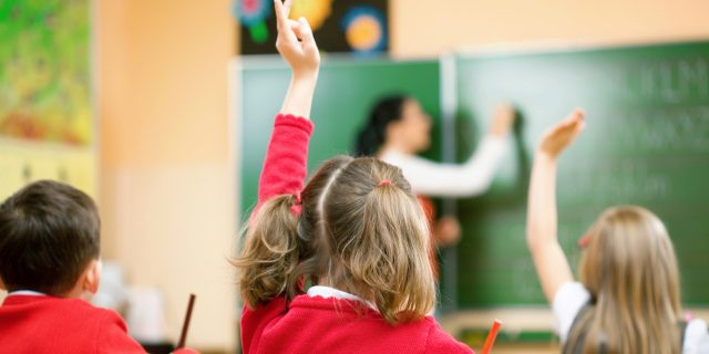 What Has Helped Me and Other Students with Visual Processing Disorder A young girl wearing a red sweater raises her hand in a classroom while surrounded by her classmates.