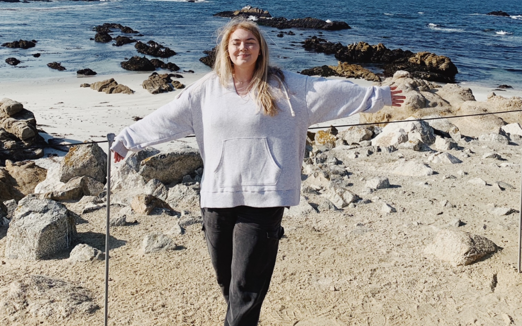 photo of Lauren Clements for ketamine infusion progress, standing at a beach with the ocean behind her, smiling