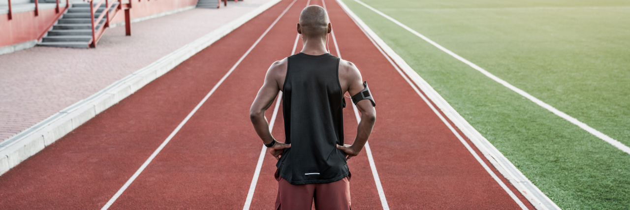 A man of color stands on the track with his hands on his hips.