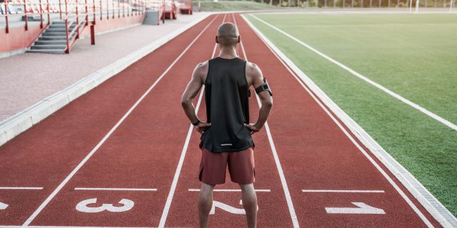 A man of color stands on the track with his hands on his hips.