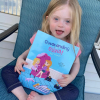 Olivia, a little girl with Down syndrome holding the children's book about her, "Outstanding Olivia."
