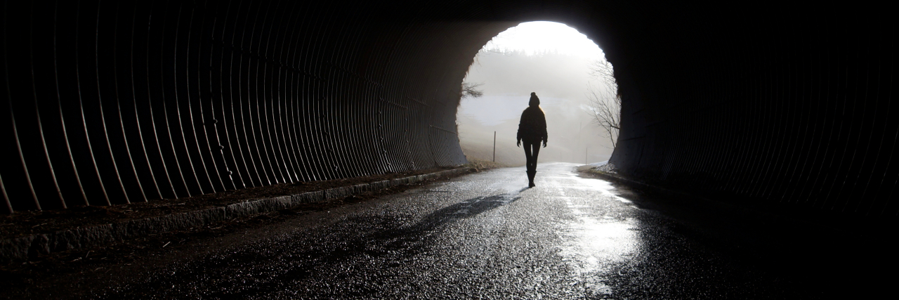 How to Get Out of a Depressive Episode A silhouette of a person walking through a dark tunnel towards a patch of light.