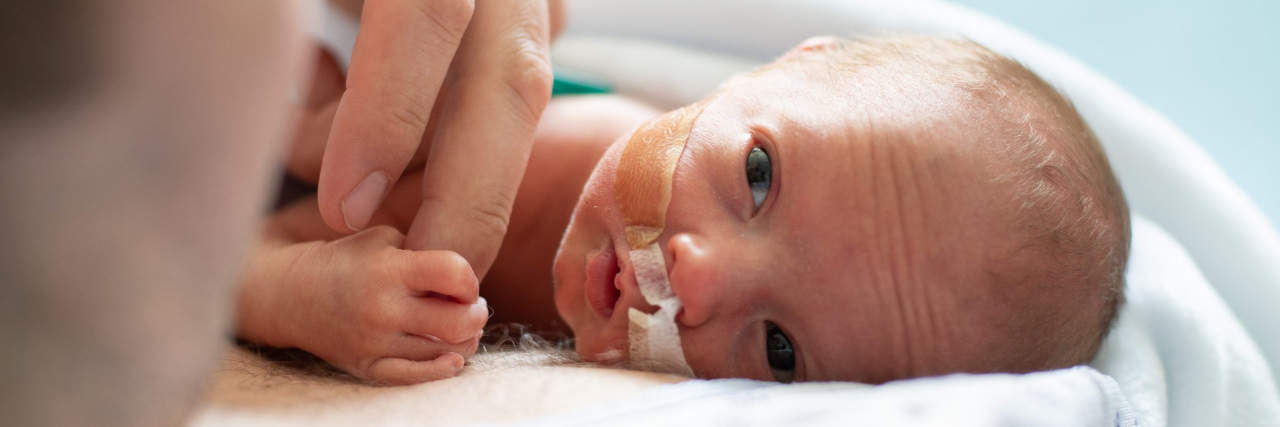 Using Adjusted Age to Calculate Premature Baby Milestones A premature baby lies on a man's chest and grips the man's finger.