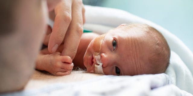 Why Considering Adjusted Age Is Important for Premature Babies' Milestones A premature baby lies on a man's chest and grips the man's finger.