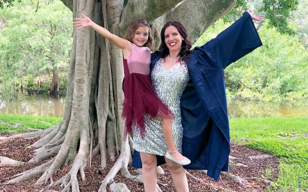 photo of Vanna Winters for ketamine infusion progress, posing for graduation in front of a tree with her daughter in her arms, both with outstretched arms