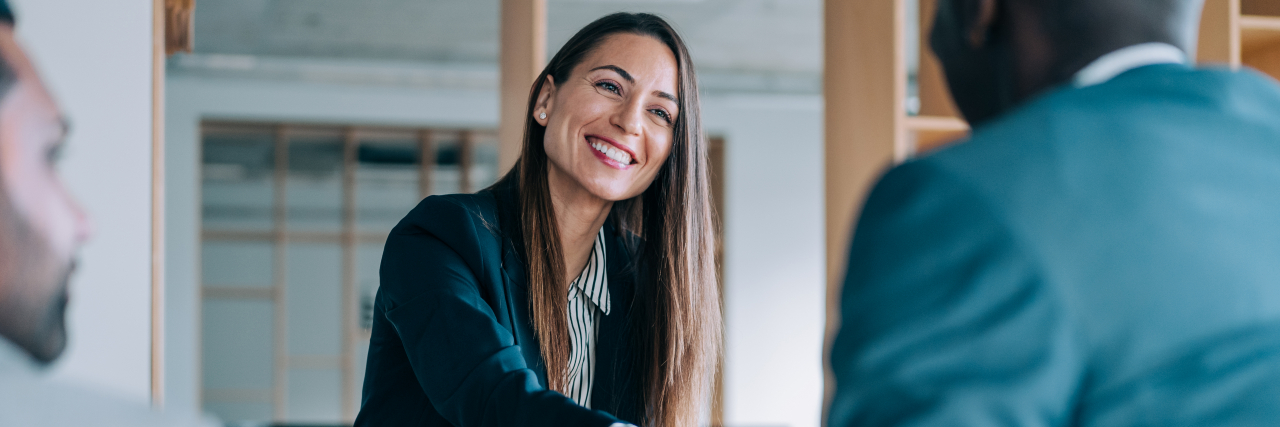 How Choosing to Disclose My Disability Empowers Me to Live Authentically A woman with long, brown hair wearing a green blazer and a button-down shirt shakes the hand of a black man.