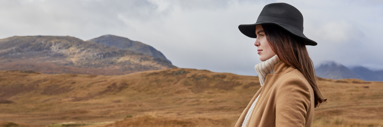 Reasons Staying Childfree Because of Health Conditions Isn't Selfish A woman with brown hair wearing a coat and hat stands in the desert.