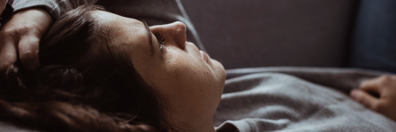 Working Full-Time With Chronic Illness and Making Choices Close-up of a woman with brown hair and brown eyes wearing a long-sleeved gray shirt and lying on a couch.