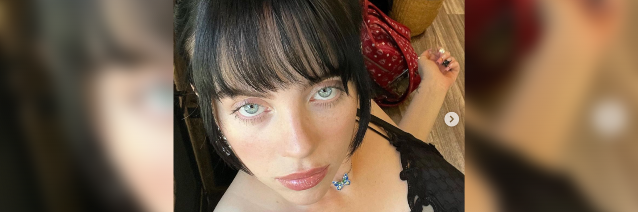 Billie Eilish Sheds Light On How Anxiety Can Show in Children Billie Eilish looking up at the camera in a black shirt with dark hair and bangs