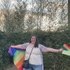 Contributor standing with her arms out holding rainbow flags