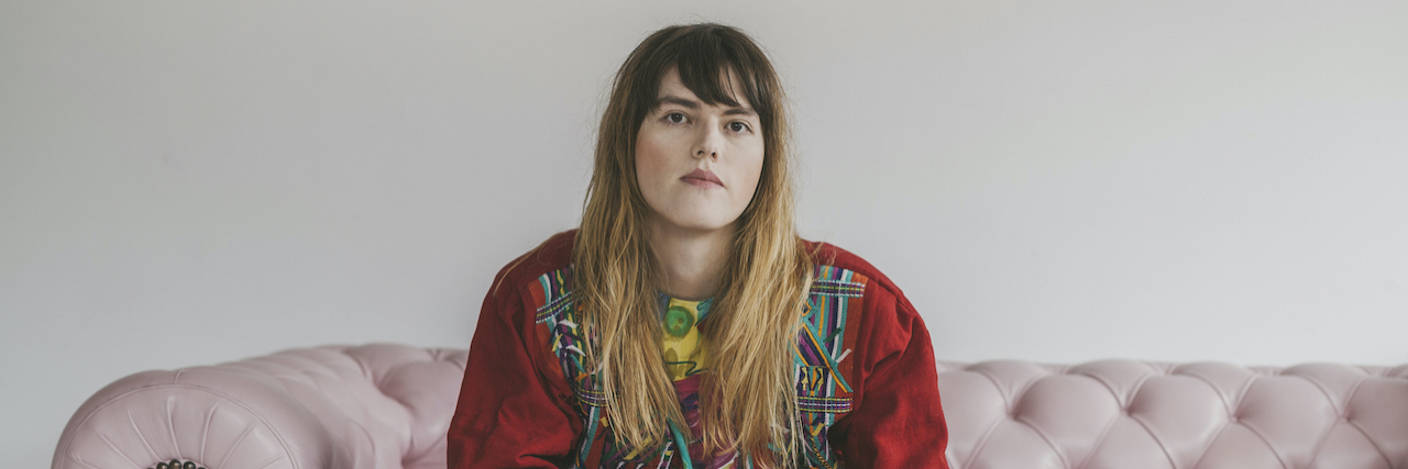 Mental Health and Addiction Treatment Needs in the Trans Community Portrait of nonbinary person with long brown hair, sitting on pink couch