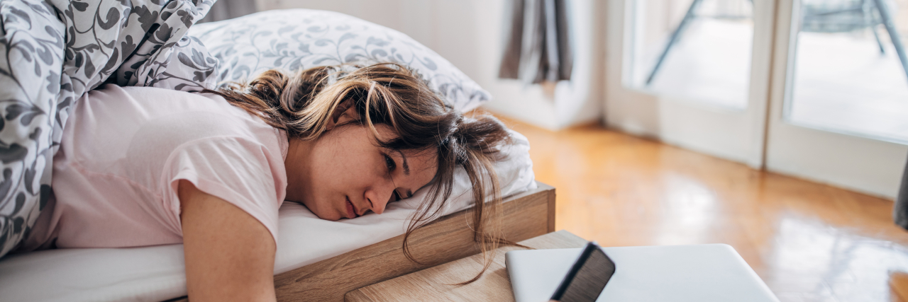 How Burnout Impacts People With Endometriosis Exhausted young woman looking at her phone while lying in bed.